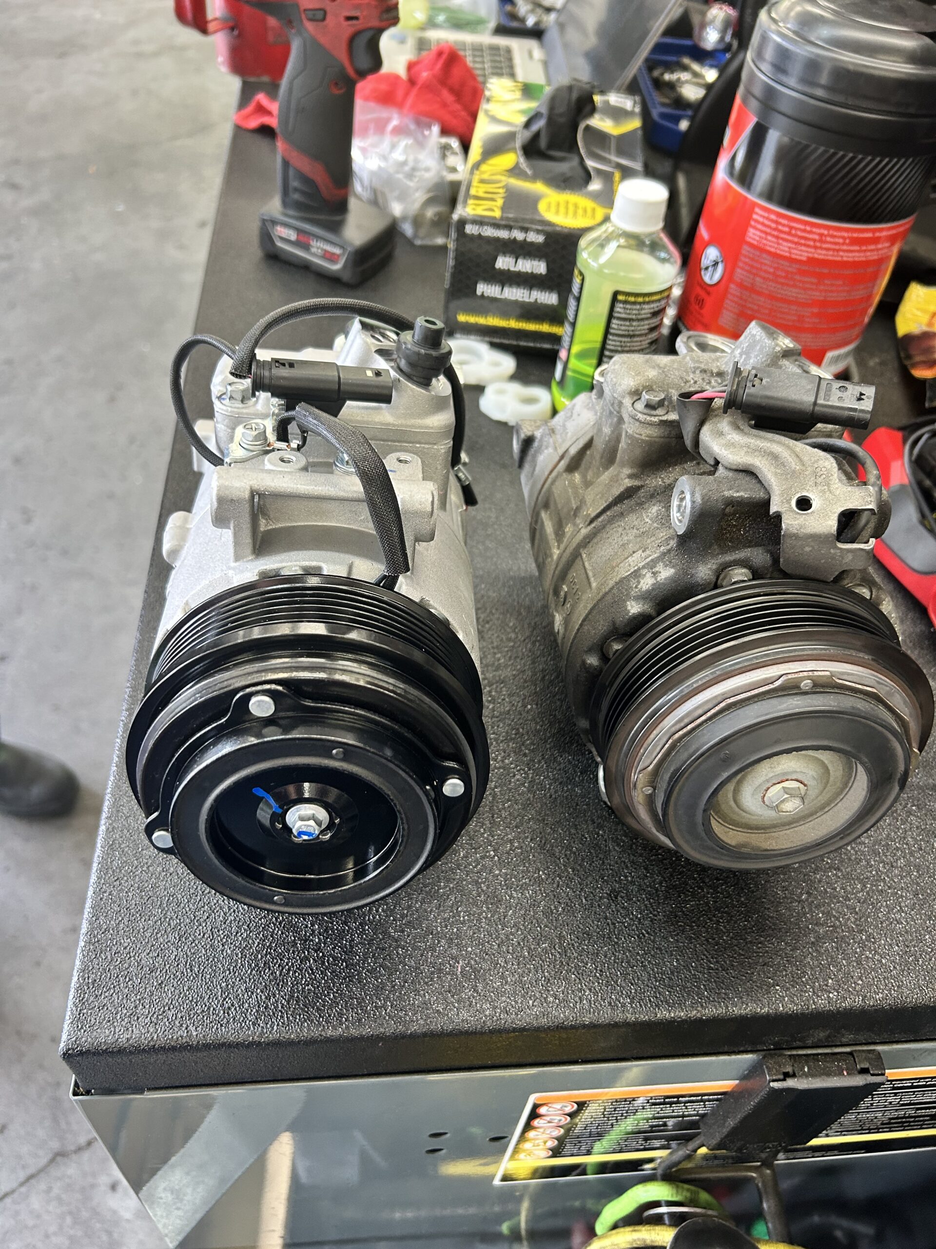 Car AC compressor replacement showing new vs old part in Houston auto repair shop