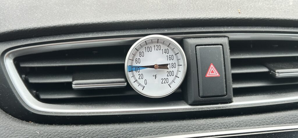 Measuring car AC vent temperature during summer inspection in Houston