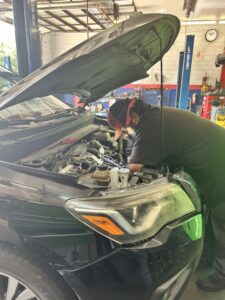 Technician performing under-hood inspection for summer car maintenance in Houston