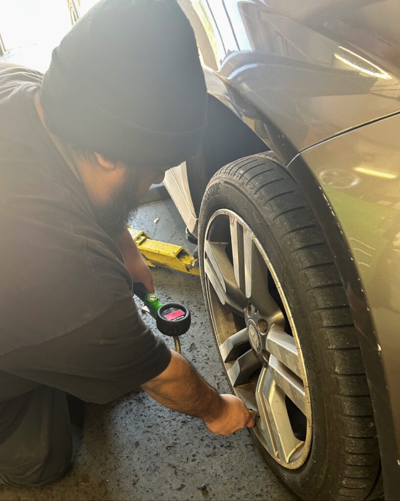 Technician checking tire pressure during summer car maintenance in Houston
